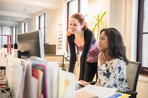 Mid adult woman is leaning on desk and young businesswoman is sitting with her hand on her chin